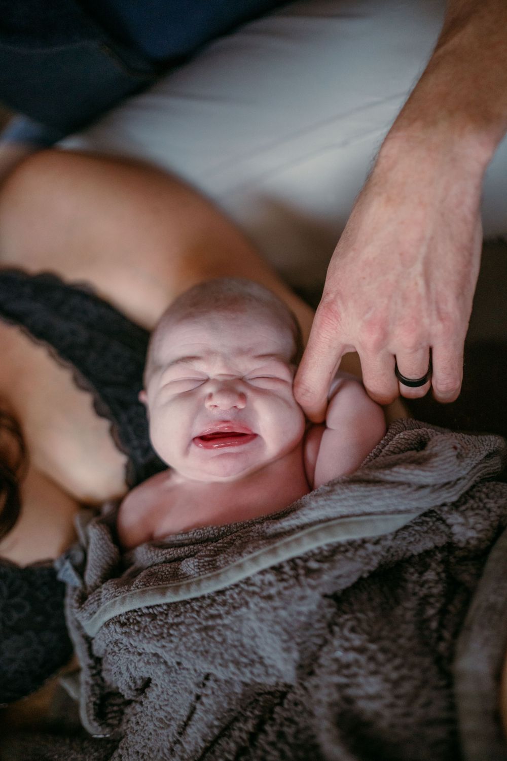 Close-up of a crying newborn baby wrapped in a gray blanket.