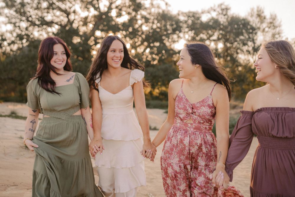 Four friends in flowing dresses walk together on a dirt path during golden hour.