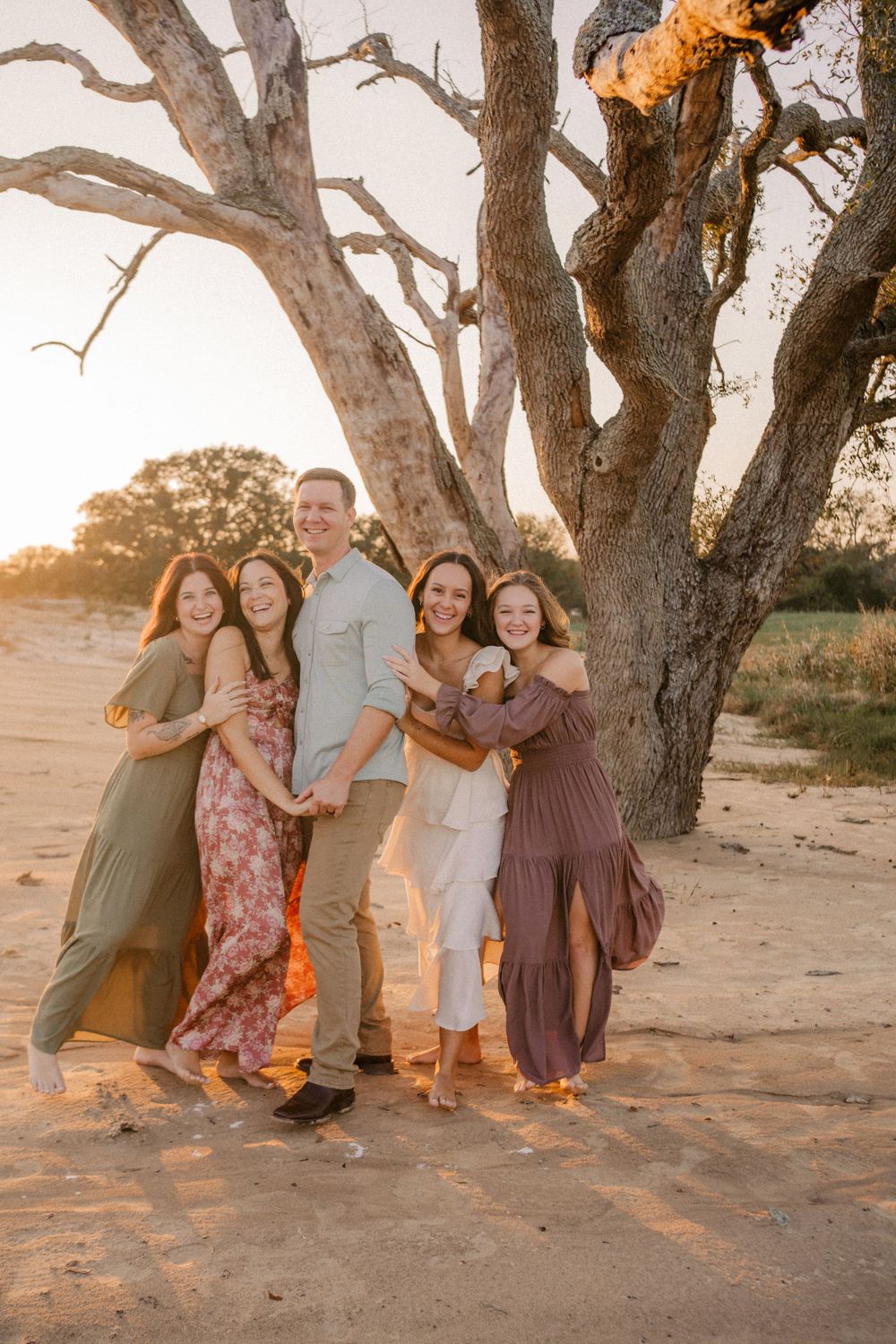 Group photo of friends posing together under a large tree at sunset.