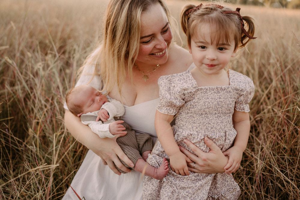 Intimate family portrait captured in a sun-drenched field with soft golden light and natural tones.