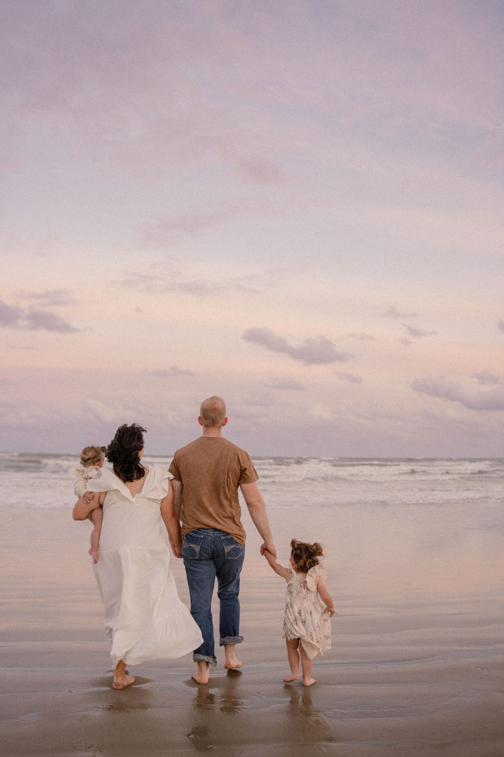 Family walking together on beach at sunset with waves rolling in.