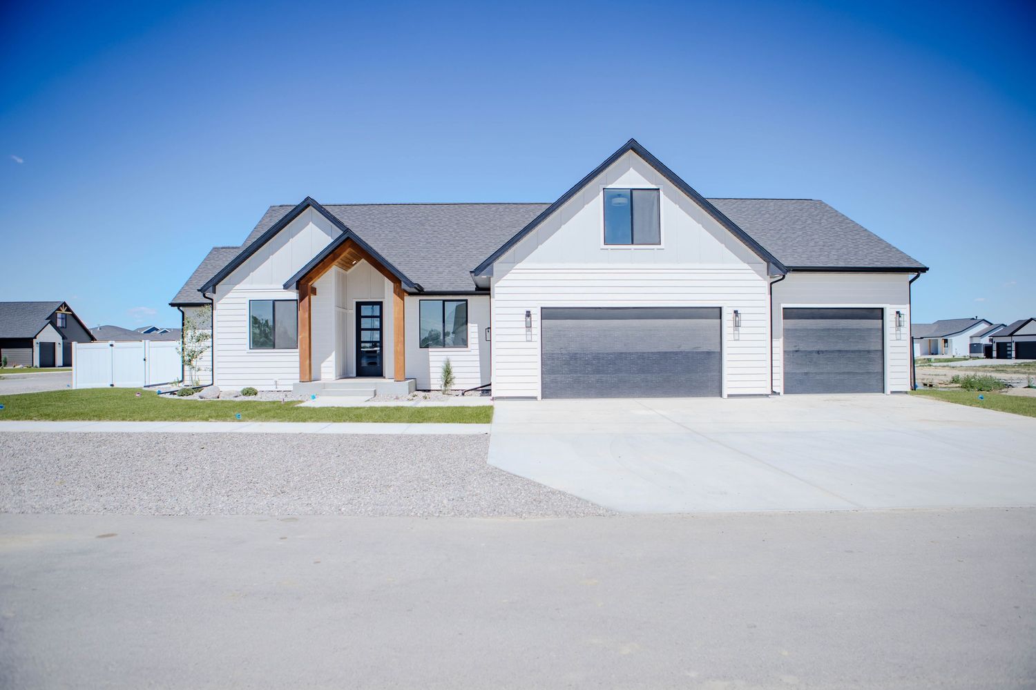 Modern craftsman style home with gray siding, three-car garage and concrete driveway against blue sky.