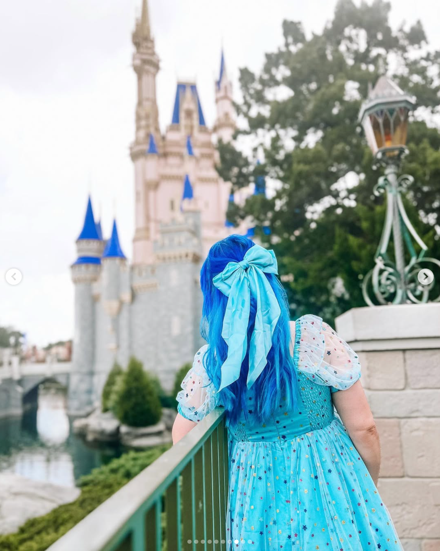 A light blue princess-style dress with puffed sleeves and delicate lace details is displayed against a castle backdrop at Disney World.