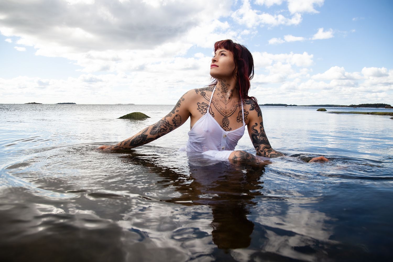 Person in a white tank top wading in calm ocean waters under cloudy skies.