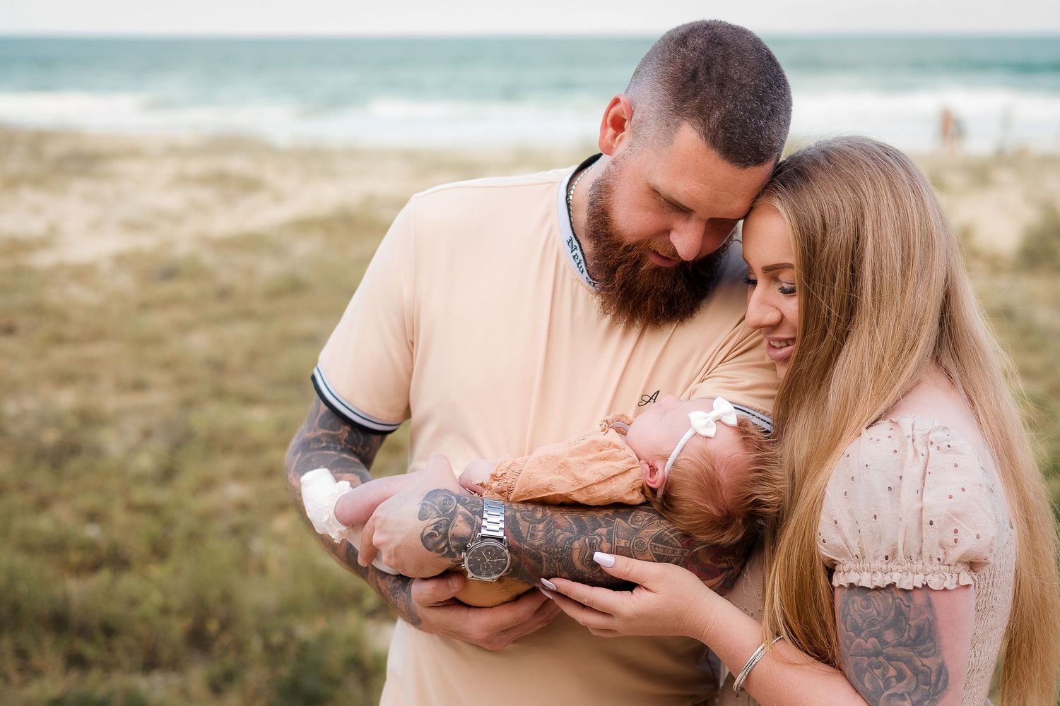 Mother and Father holding their newborn baby in a tender moment of love at the beach in the Sunshine Coast