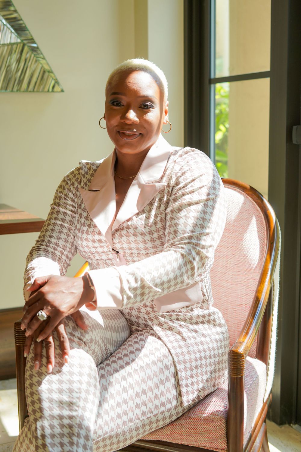 Woman in white patterned dress sitting comfortably in chair by window.