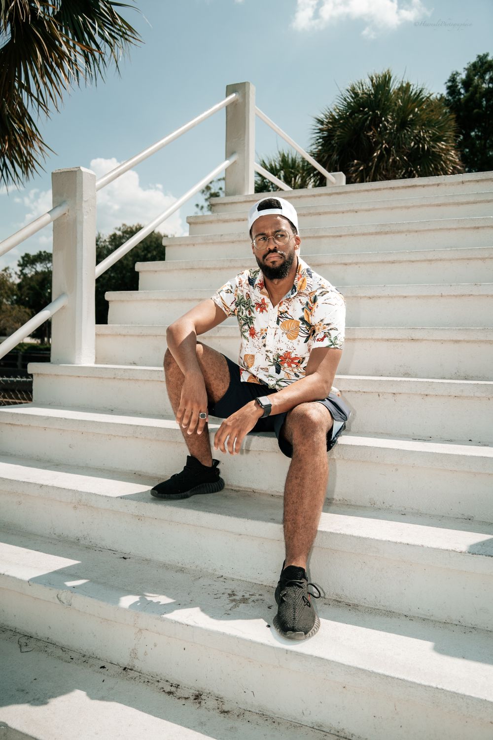 Person in floral shirt relaxing on white concrete steps outdoors.