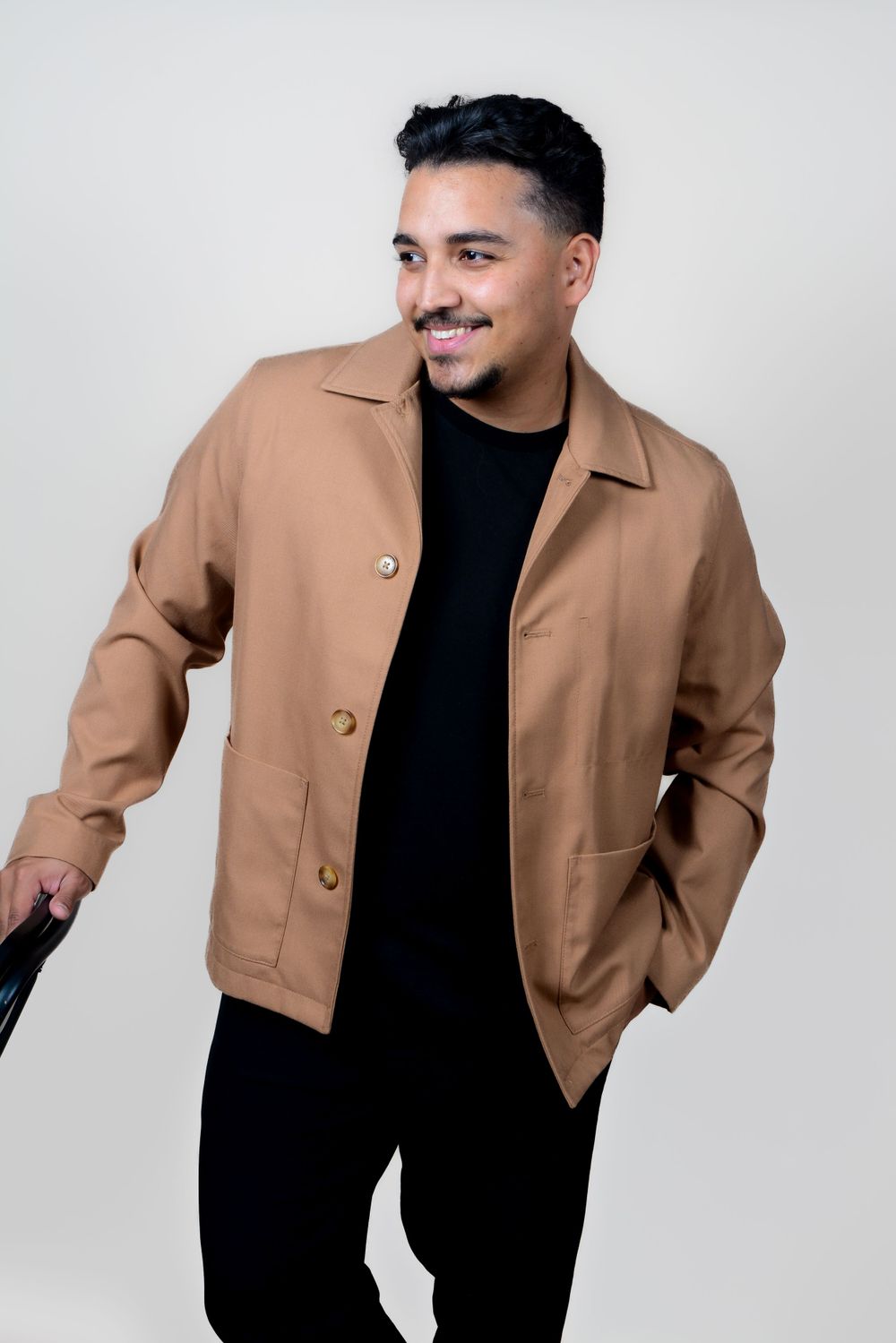 Man modeling tan jacket and black turtleneck in professional studio photoshoot.