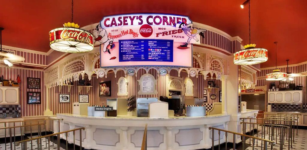 Interior view of Casey's Corner restaurant with vintage-style counter, neon signs and red walls in Disney theme park setting.