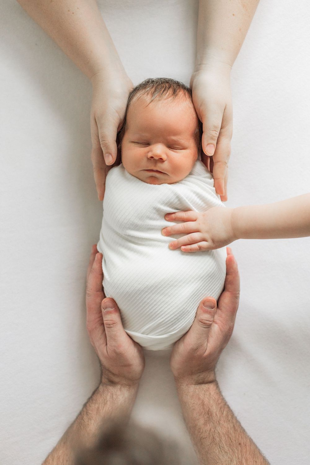 A sleeping newborn in white onesie held gently by caring hands against white background.