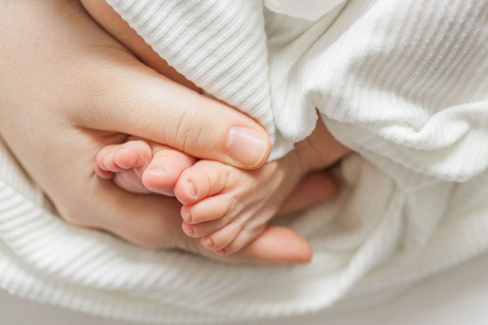 A tiny baby hand gently rests on an adult hand against soft white fabric.