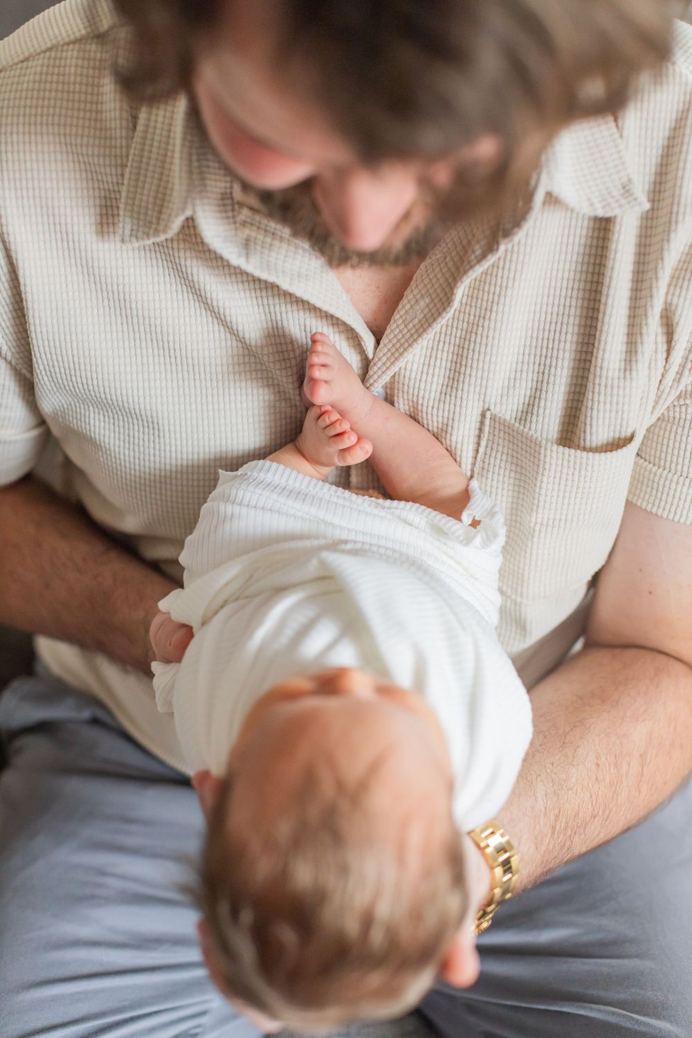 A tender moment shows a baby's tiny feet being gently held while swaddled in white fabric.
