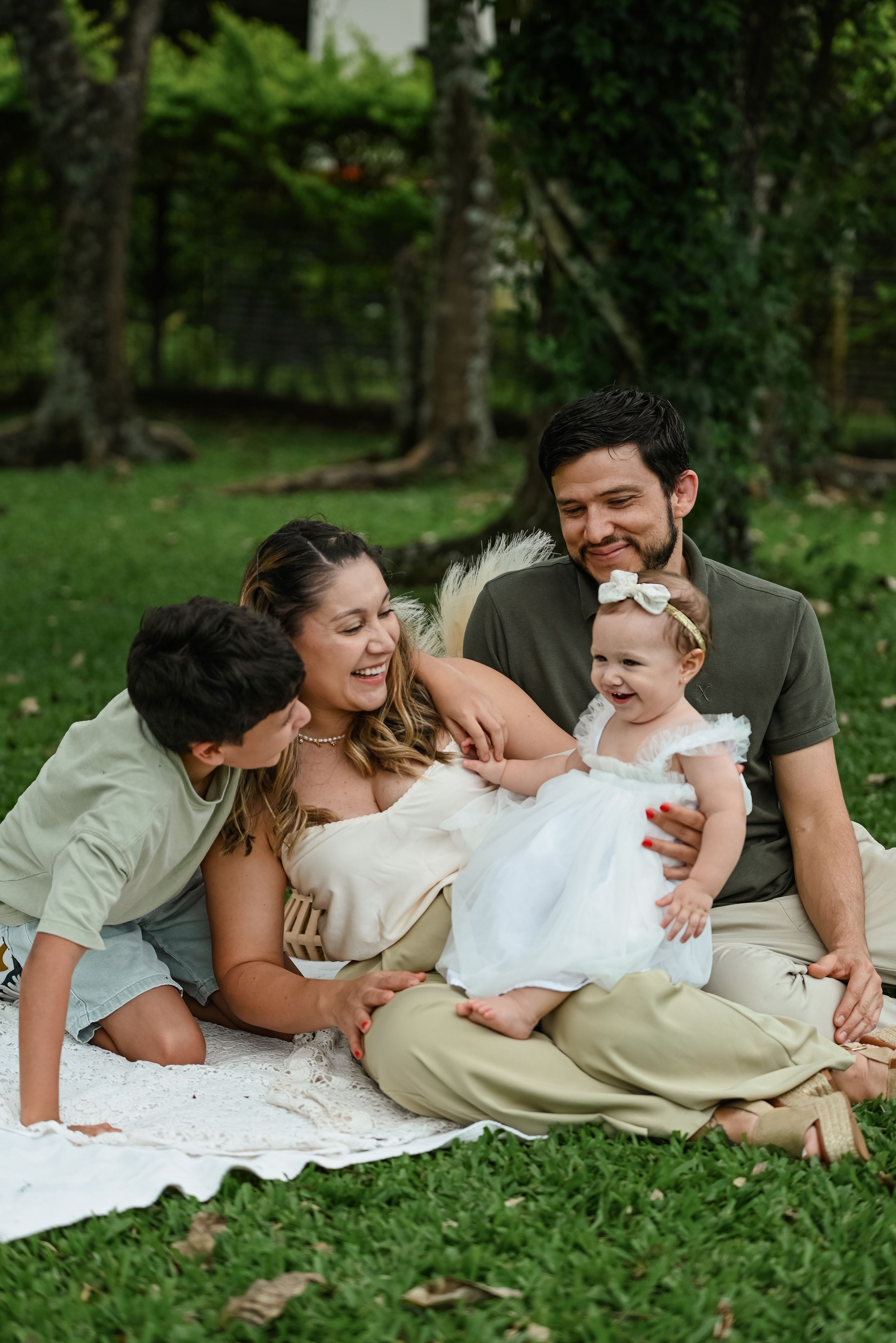 Family sits together on white blanket having intimate moment on grass during outdoor photo session.