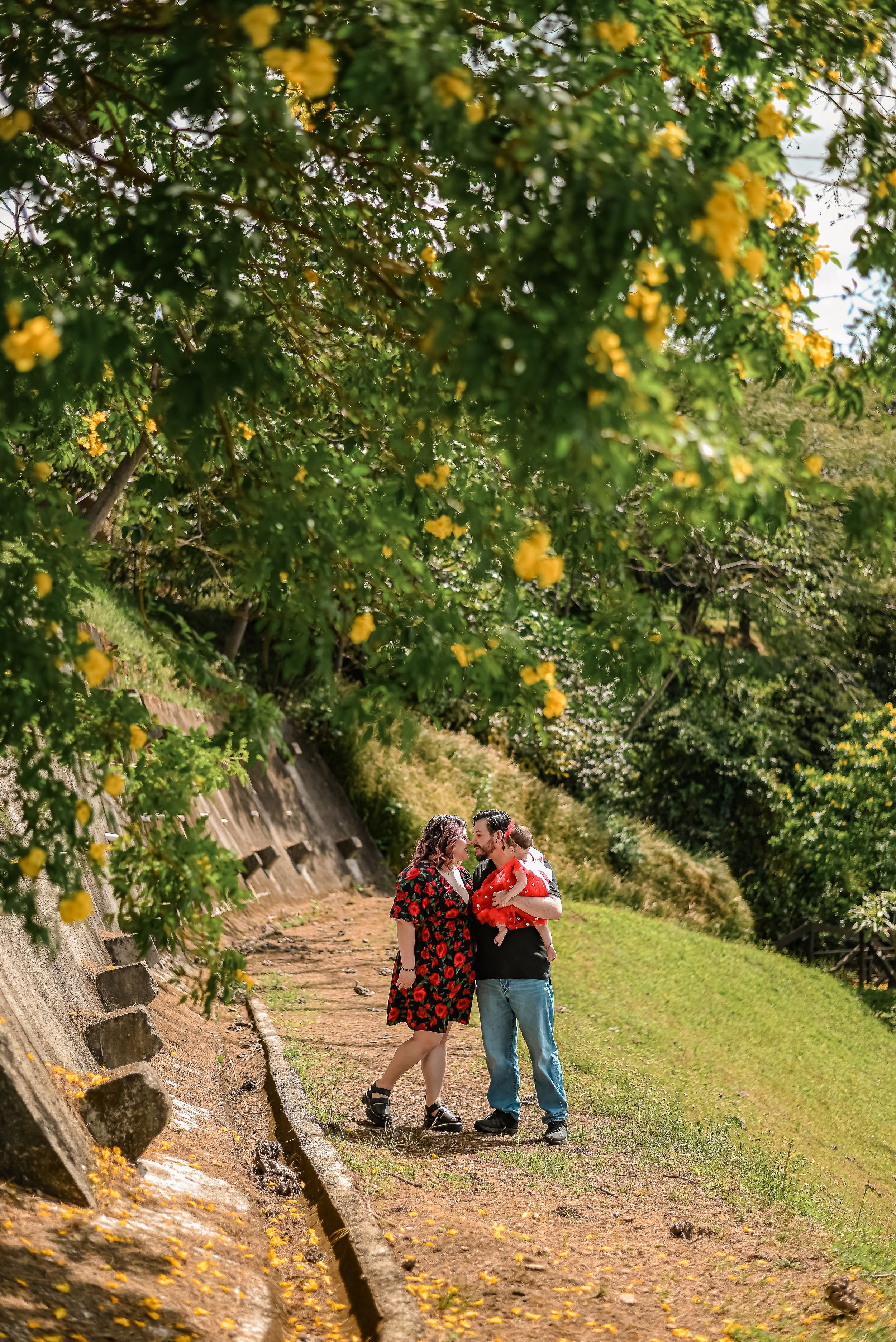 A couple embraces on a scenic autumn path under blooming yellow flowers and lush green trees.