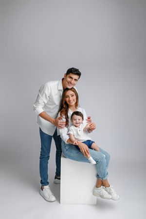 Happy family dressed in white and jeans sitting and standing against gray background in studio setting.