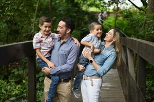 A family sharing joyful moments together while standing on a wooden bridge in a green forest setting.