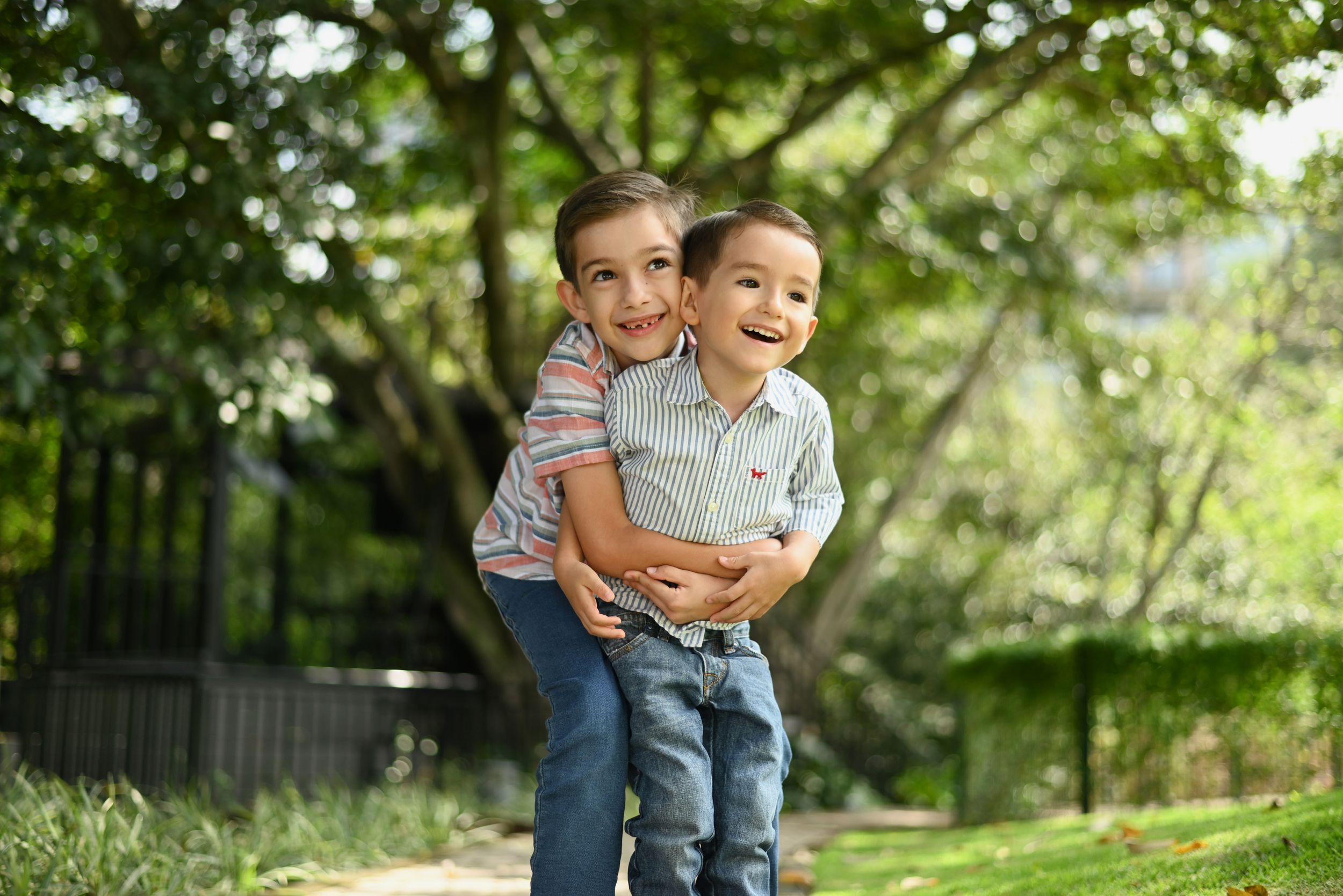 Two siblings embracing and laughing together in a sun-dappled garden setting on a bright summer day.