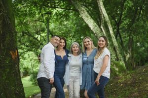 A group of five people pose together outdoors in a wooded area with lush green trees in the background.