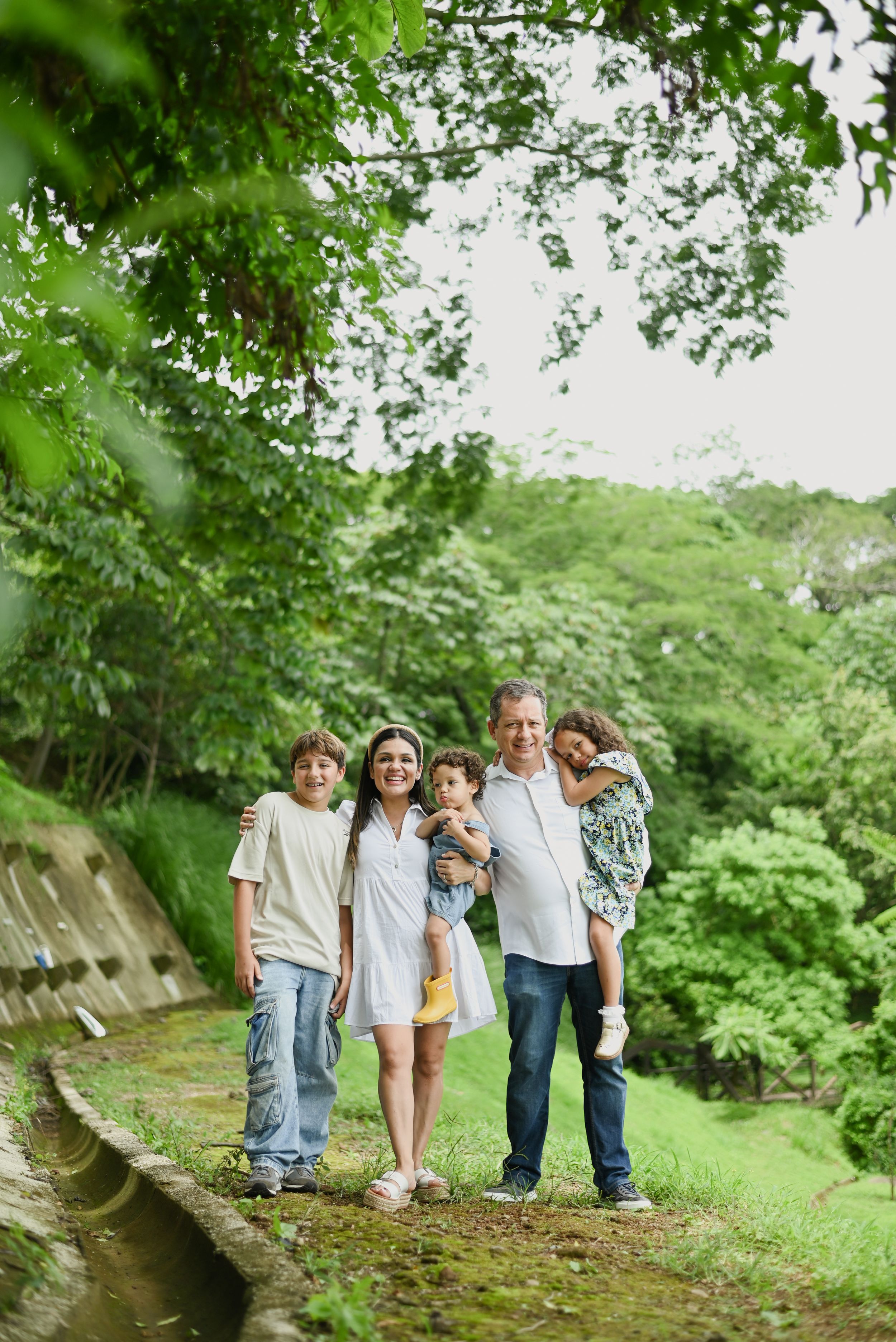 A family group walking together on a green woodland path surrounded by lush summer foliage.