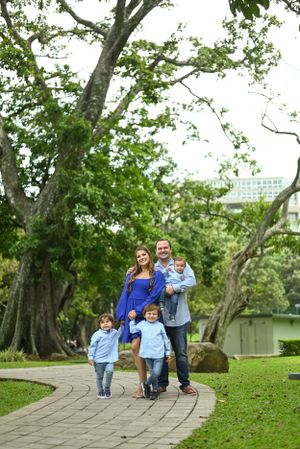 A family walks together on a curved stone path through a lush green park on a pleasant afternoon.