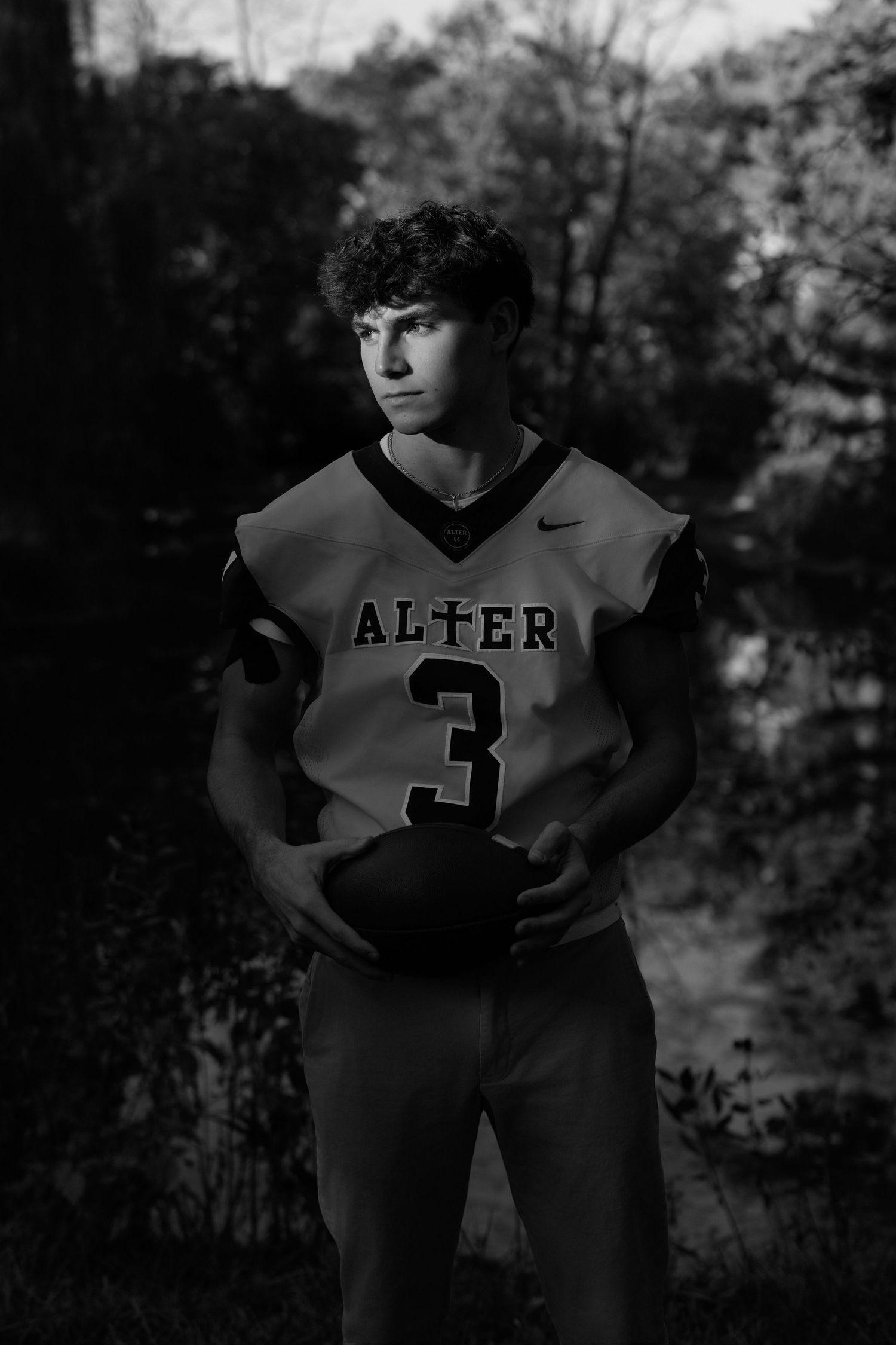 Black and white portrait of an athlete in an Alter #3 Nike jersey holding a basketball outdoors.
