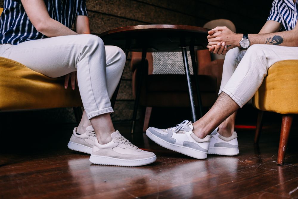 Two people sitting in yellow chairs wearing white sneakers and white pants on a wooden floor.
