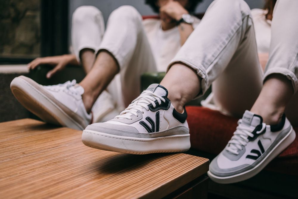Multiple pairs of white athletic shoes with black V logos sit on a wooden surface, showing casual sporty style.