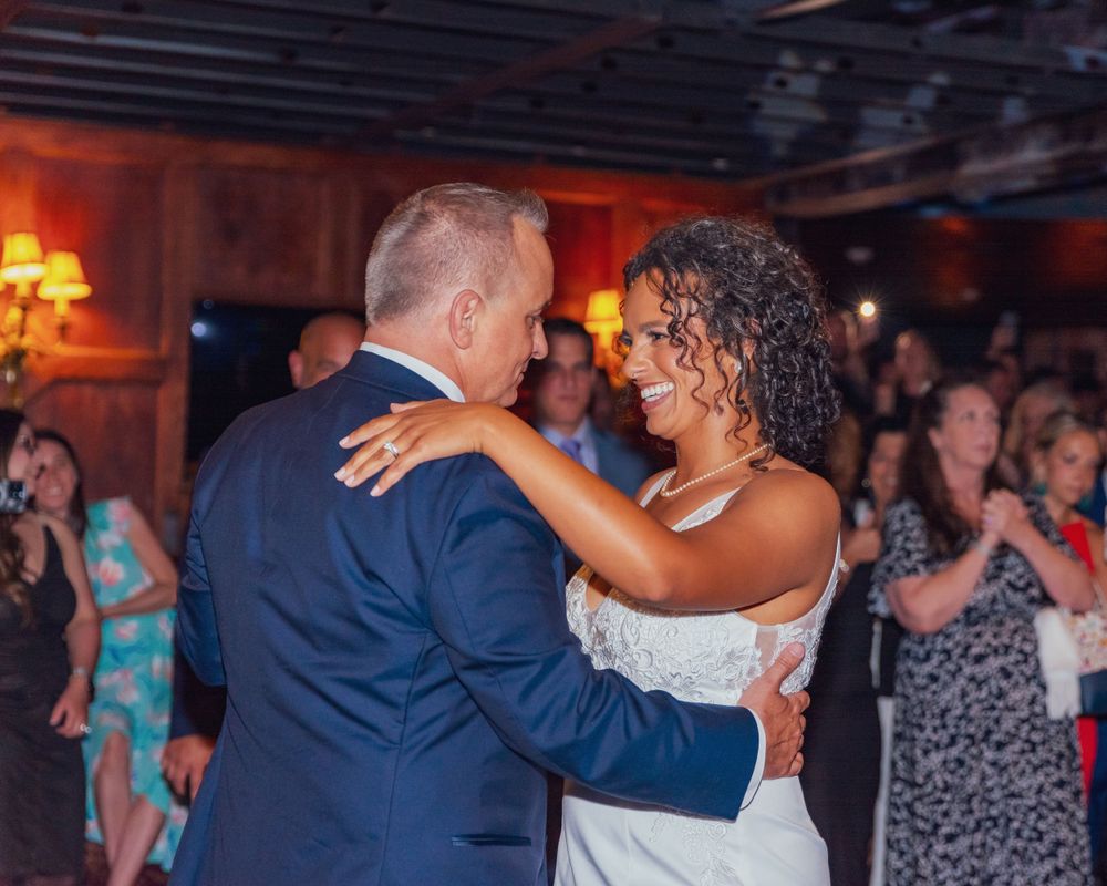 A couple shares a joyful moment while dancing together at an indoor wedding reception with warm lighting.