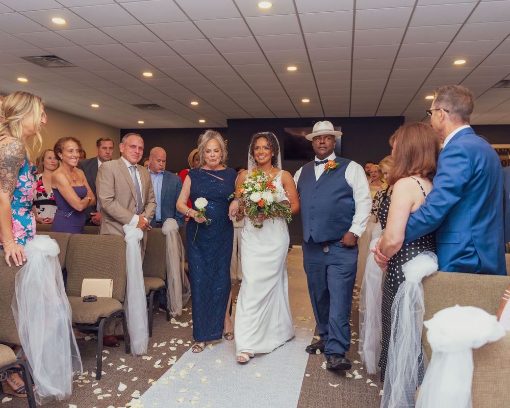 Wedding ceremony with aisle lined by wedding party in navy blue and neutral tones with scattered petals on the floor.