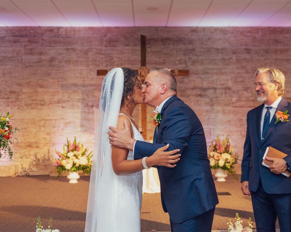 A wedding ceremony in front of a brick wall decorated with warm lighting and floral arrangements.