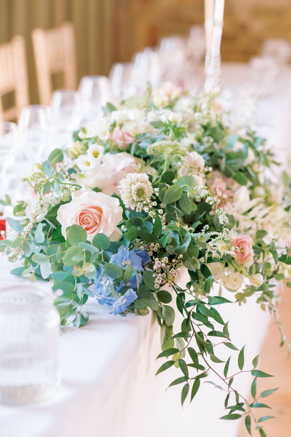 Elegant wedding table centerpiece features soft pink roses, delicate blue flowers and cascading eucalyptus greenery.