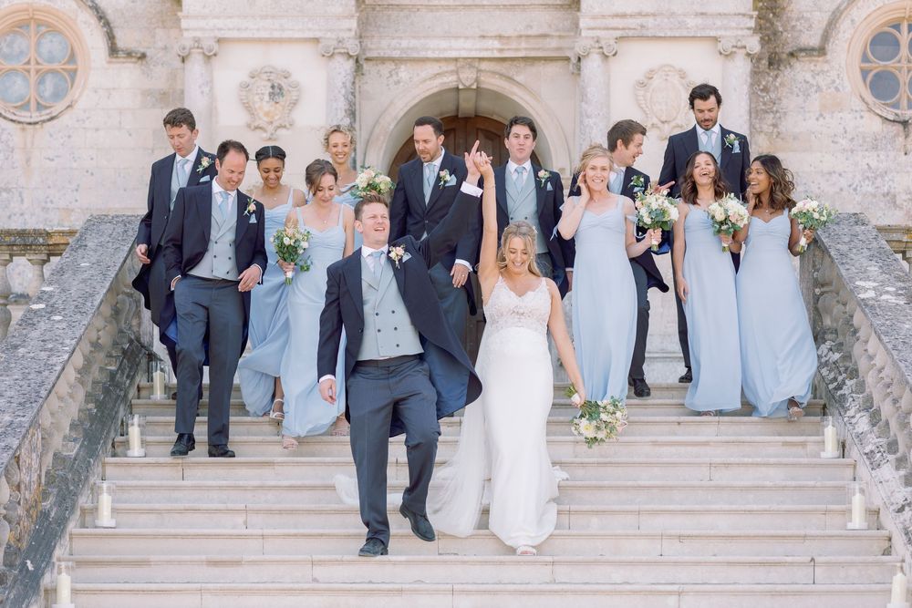 Wedding party standing on grand stone steps of a historic castle building in a formal group photo.