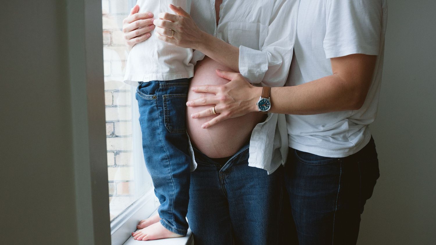 Family looking out of the window while the dad is touching the mom's pregnant belly, detail shot from a family maternity session in Vancouve