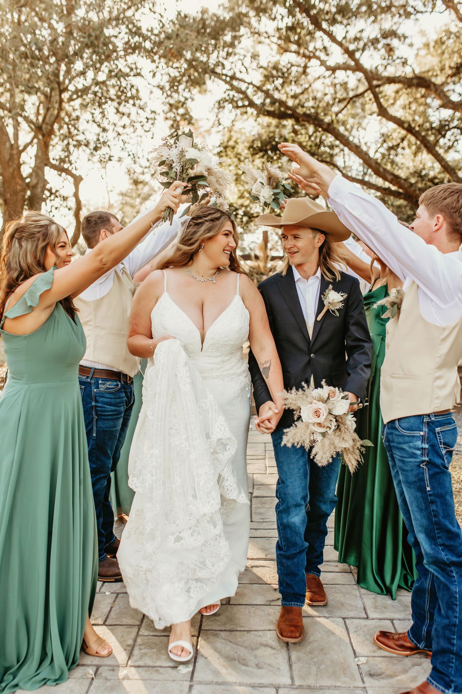 Festive wedding celebration with guests creating arch over couple on stone pathway.
