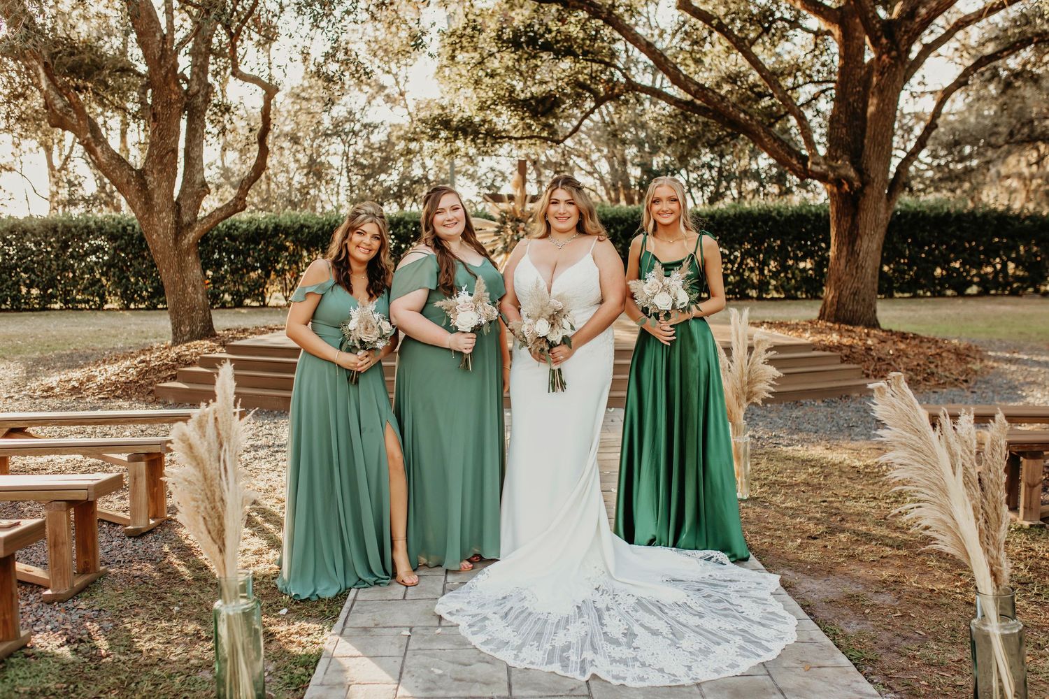 A wedding party poses together on a paved garden path surrounded by oak trees.