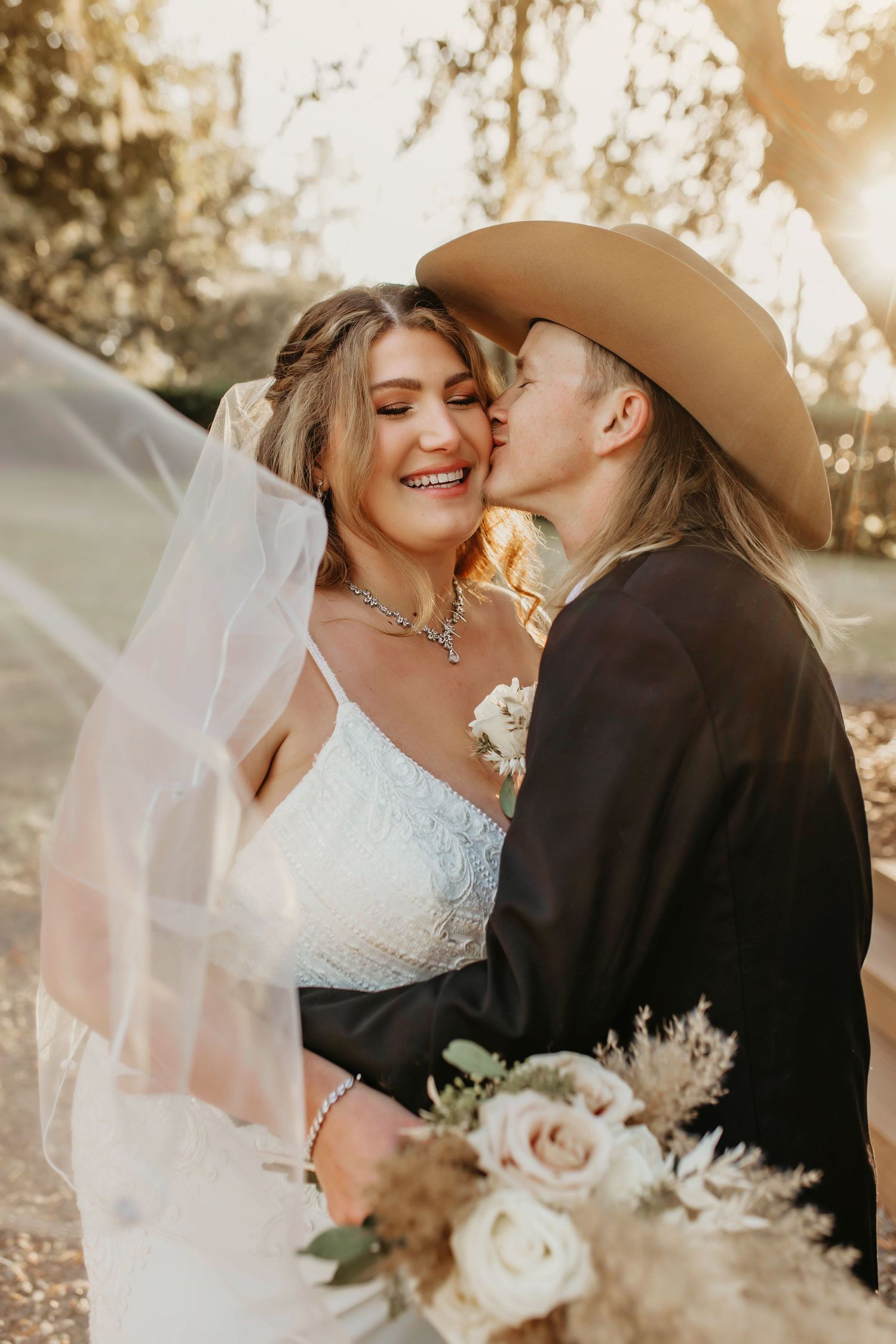 Romantic sunset wedding portrait with couple embracing among trees.
