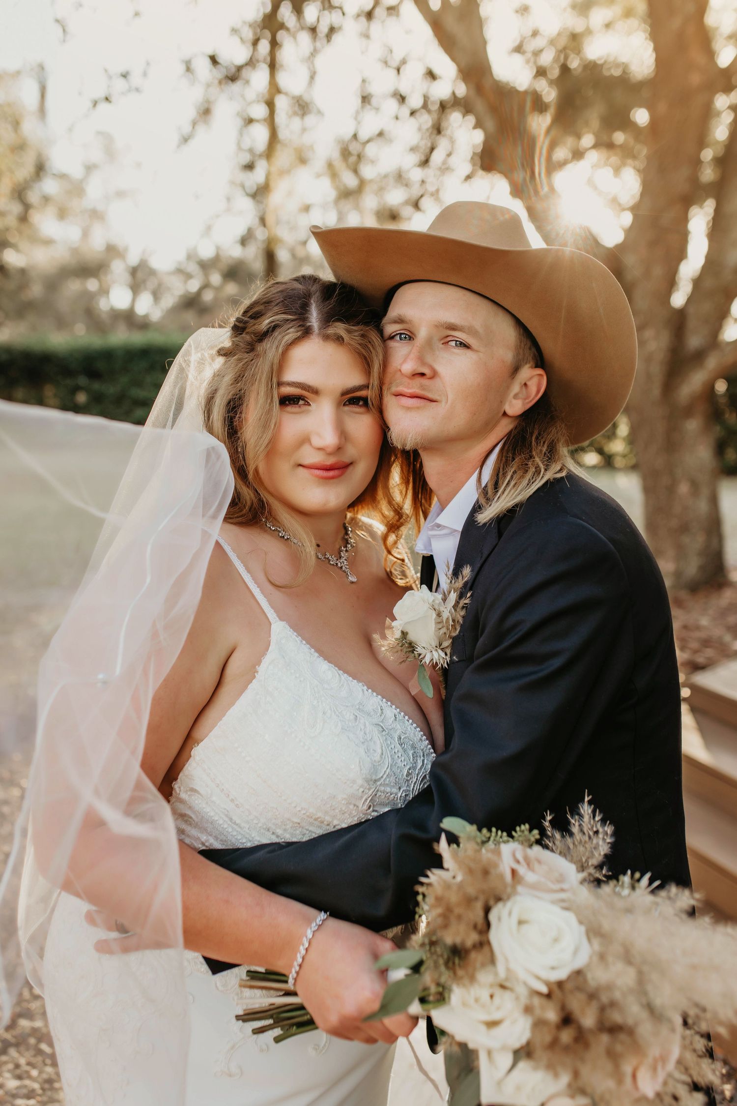 Romantic sunset portrait of couple with flowing veil and western attire.