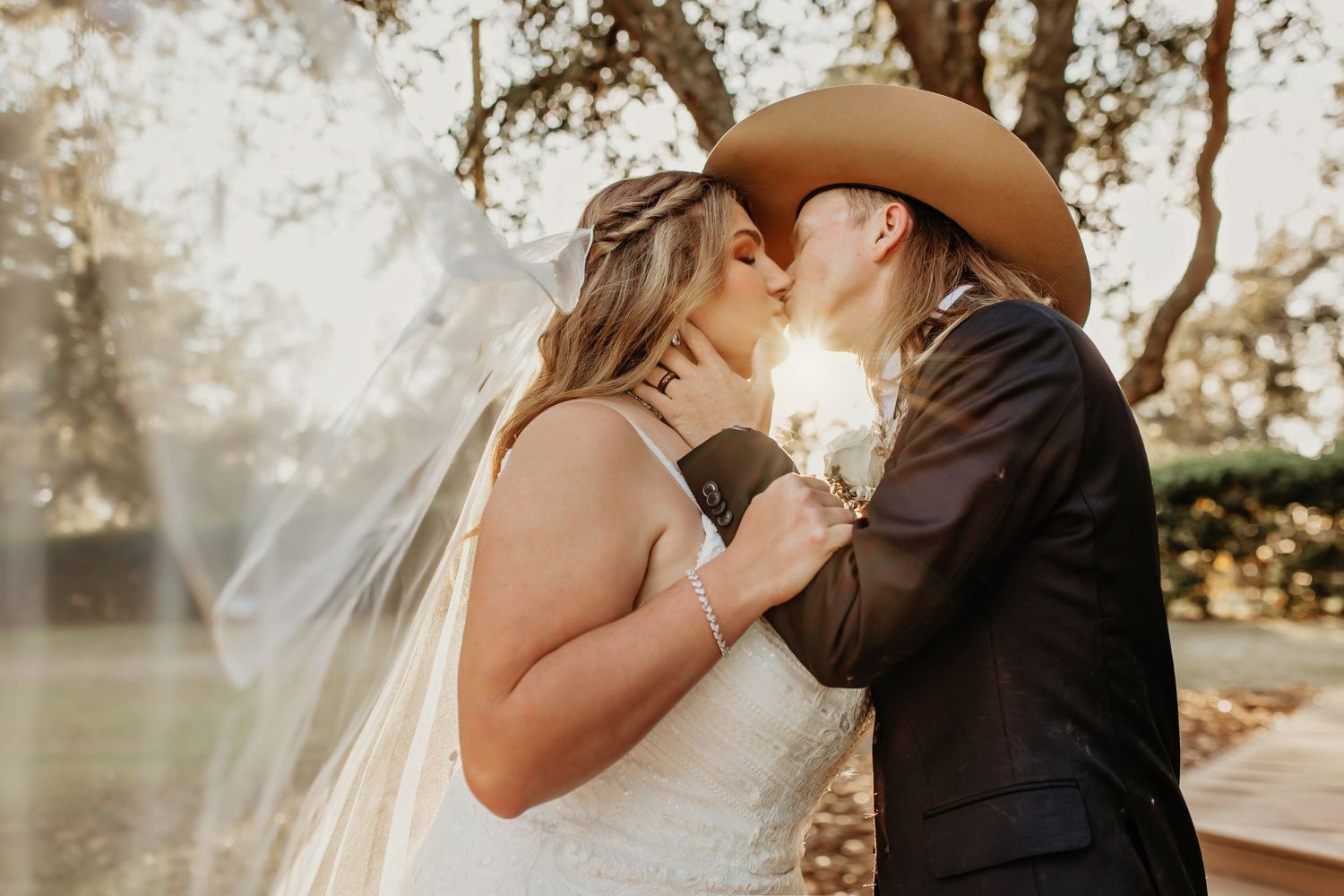 Sweet wedding moment captured at golden hour with veil flowing in sunlight.
