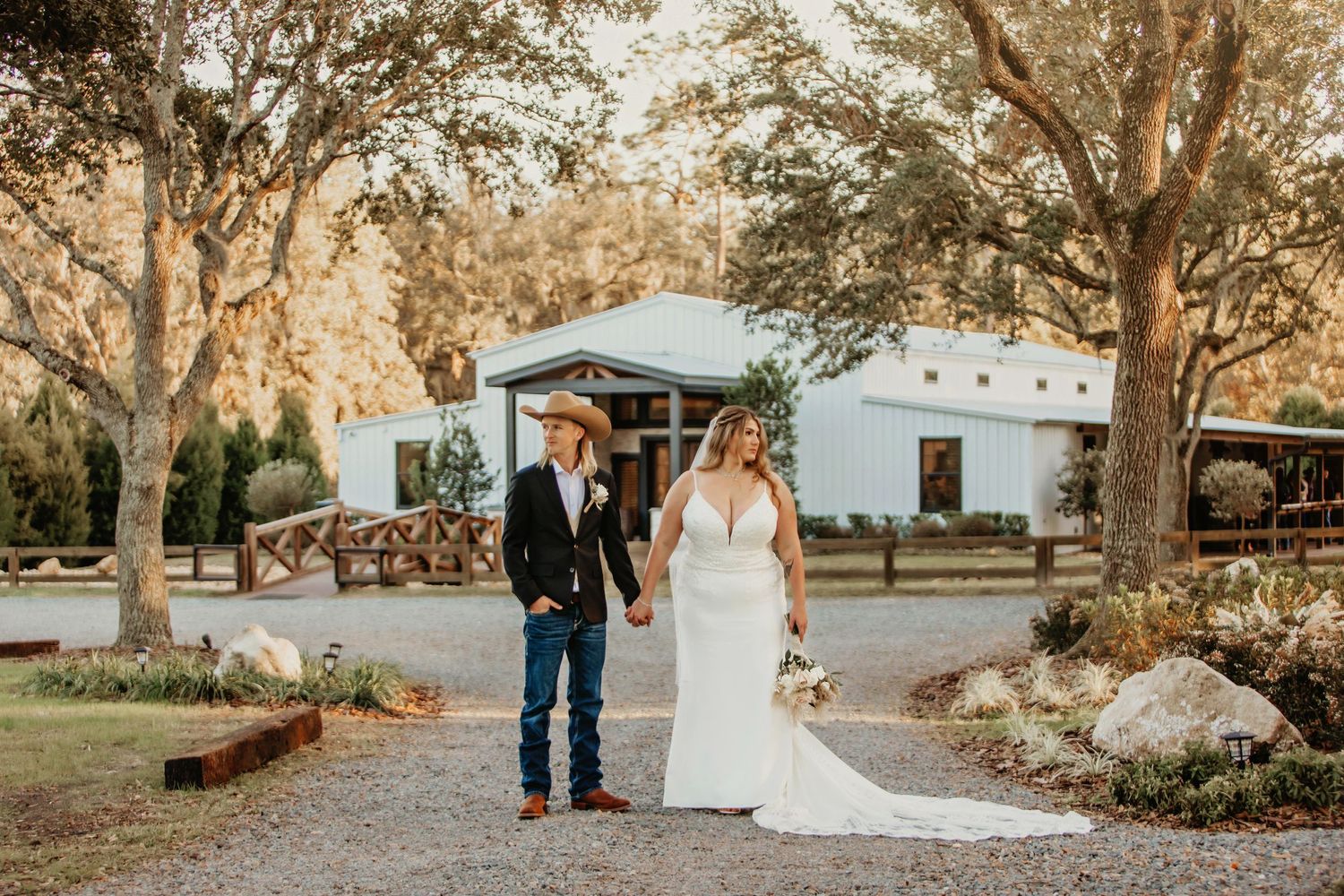 A couple walks together on a gravel path with a white building in the background.