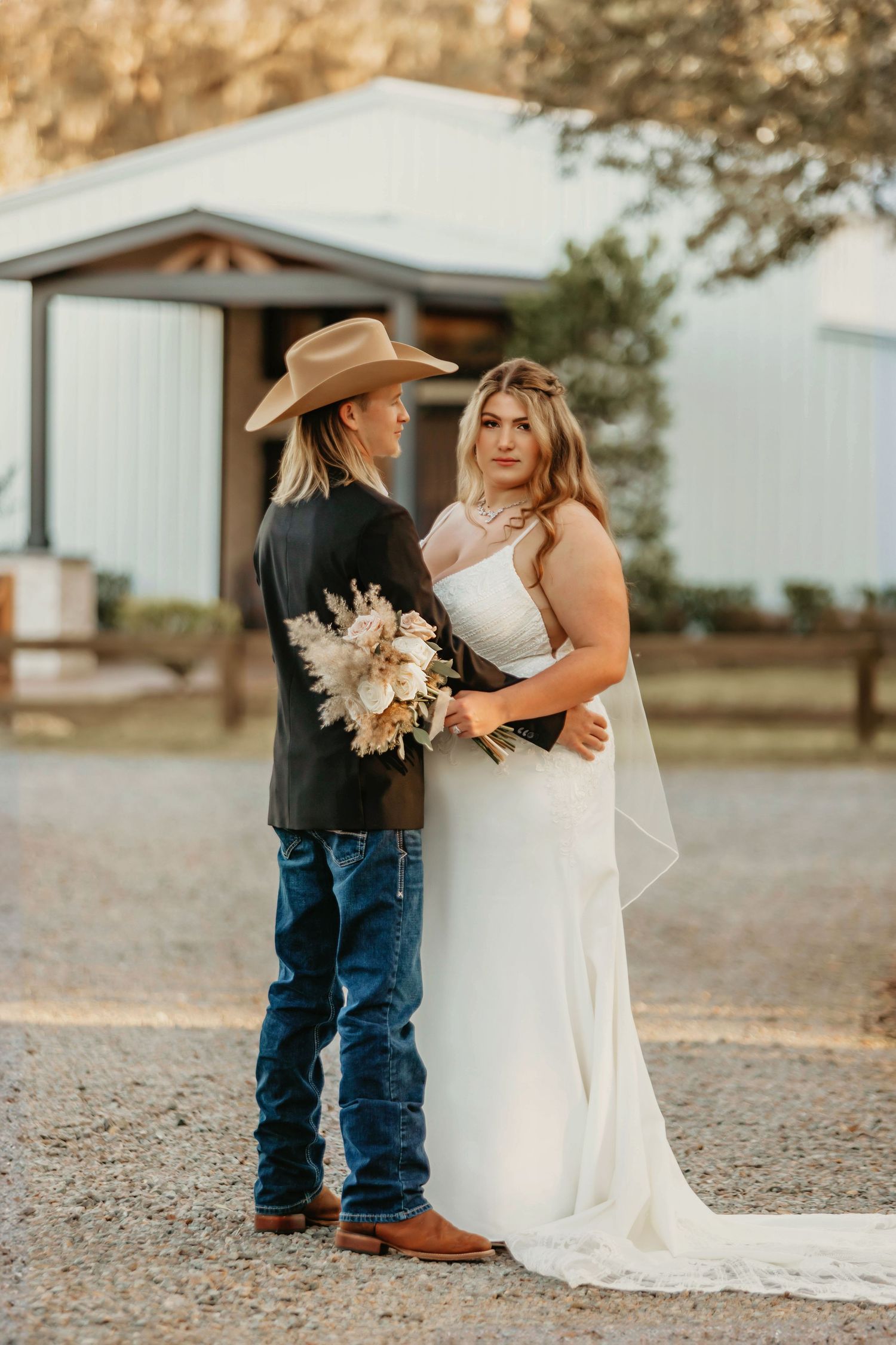 A rustic country wedding couple poses together outdoors near a white barn.