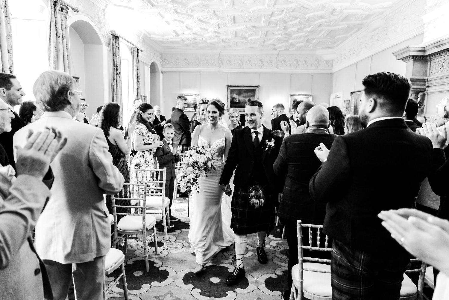 A black and white photograph capturing guests dancing and socializing at an elegant indoor wedding reception.