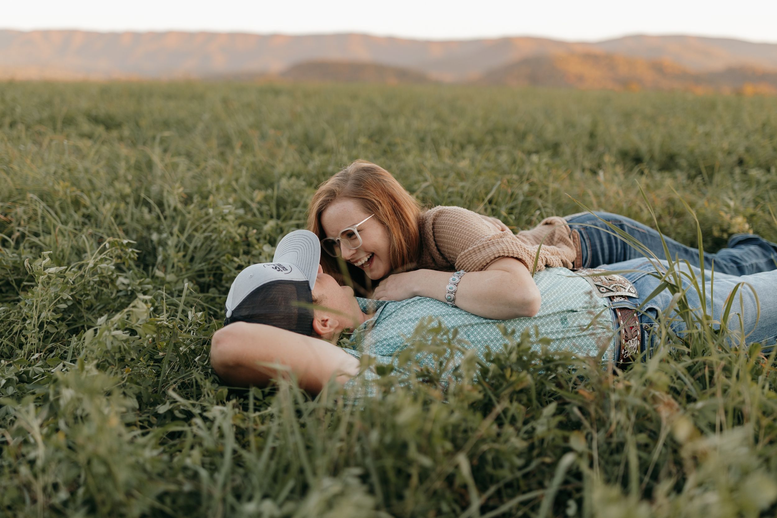 A couple relaxes together in a lush green field during golden hour.