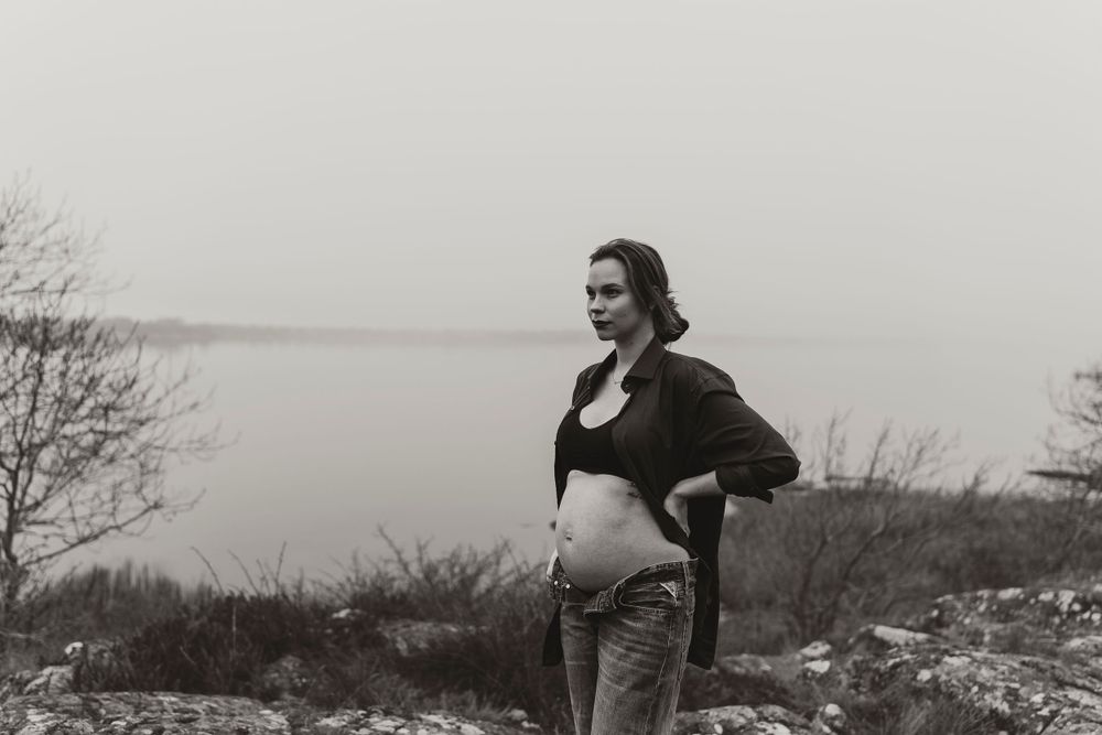 Black and white maternity photo overlooking misty waterfront landscape.