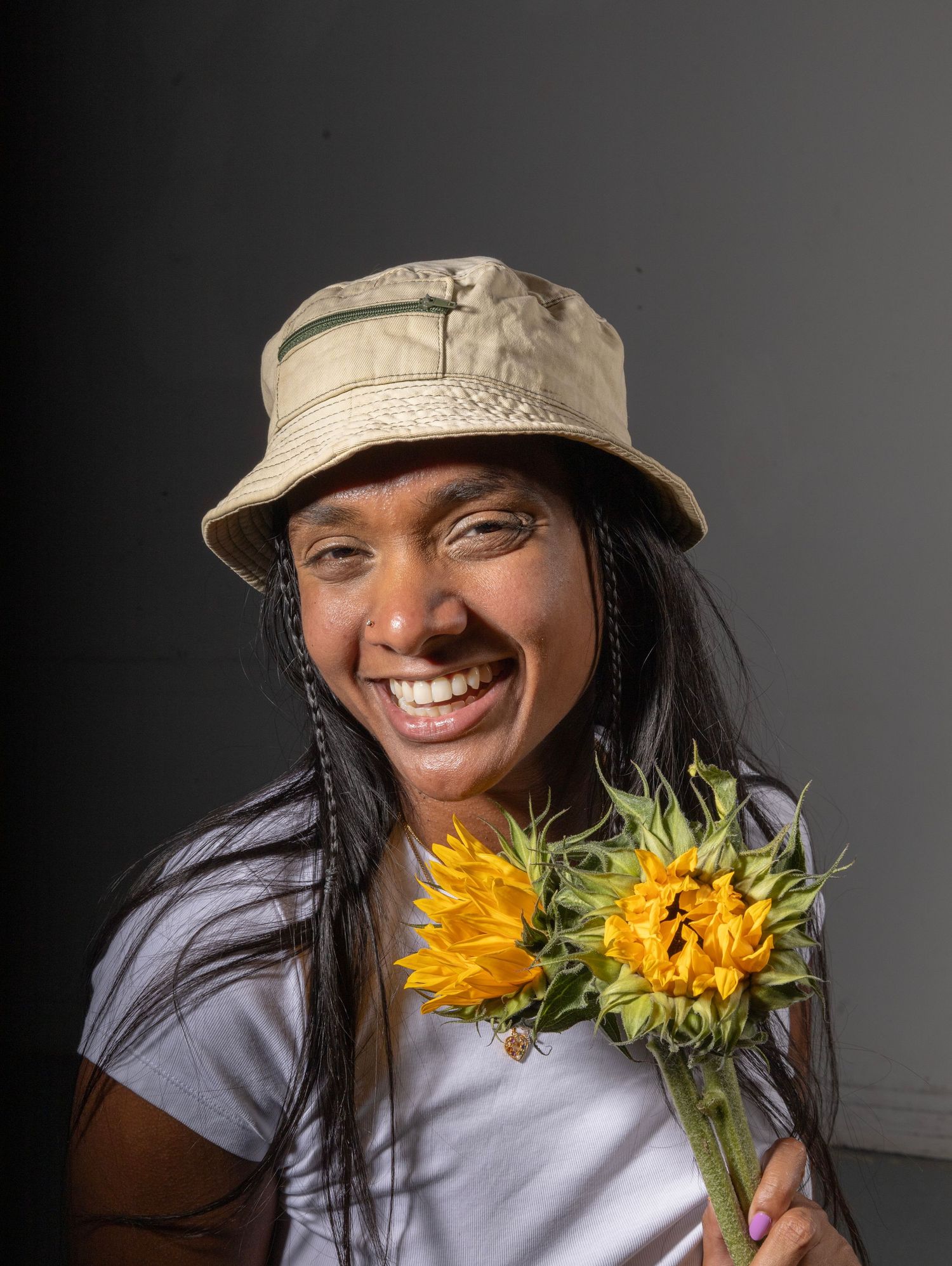 Portrait of a woman in a bucket hat holding sunflowers with a joyful expression.