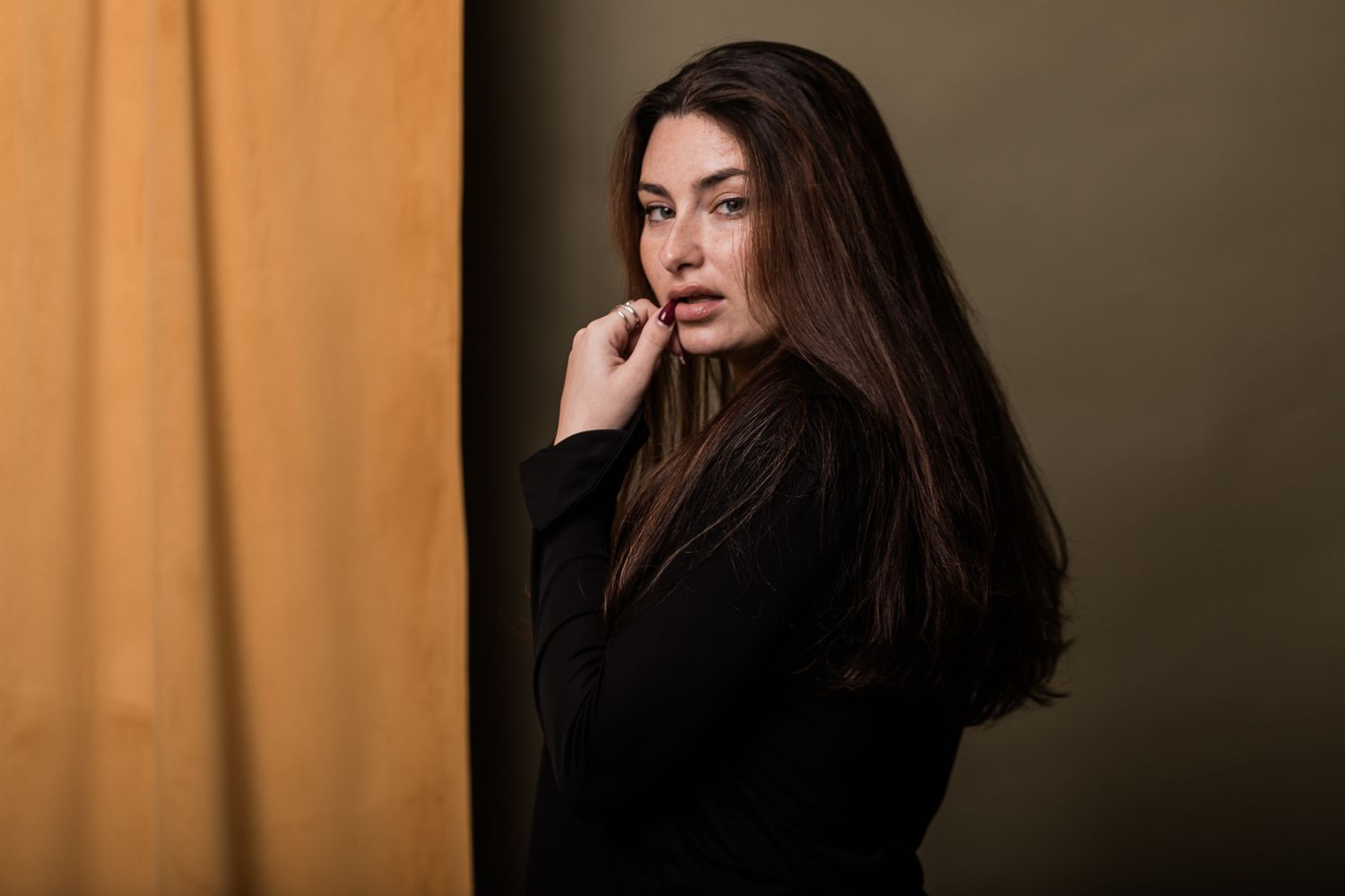 A woman in a black sweater poses with long dark hair against an orange and dark backdrop.