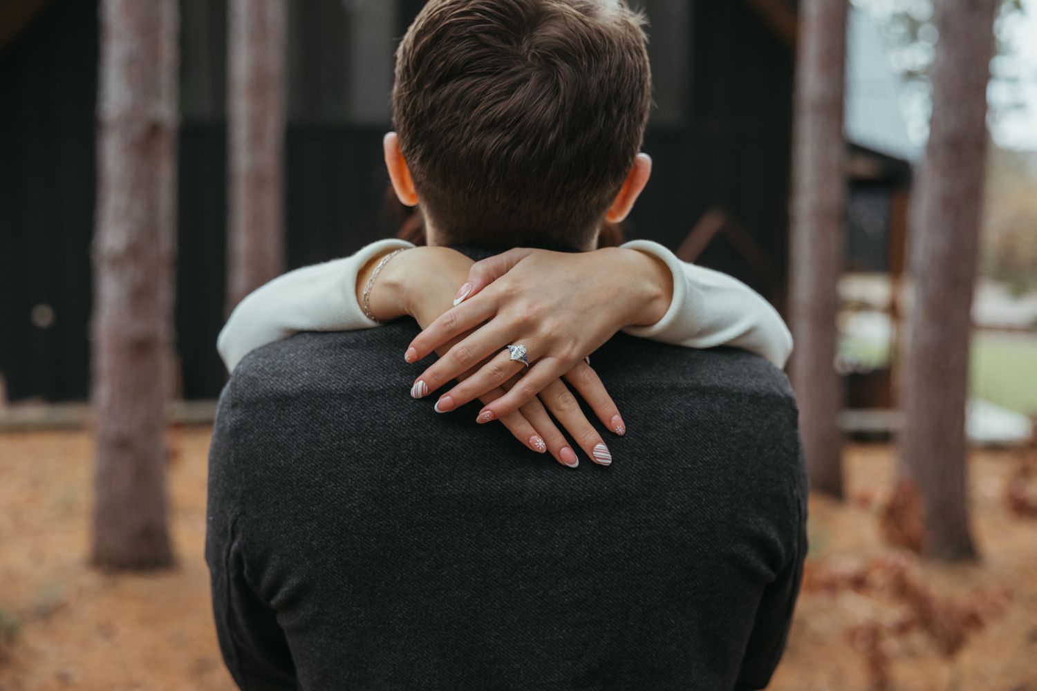 A view from behind showing someone wearing a black sweater being hugged in a forest setting.