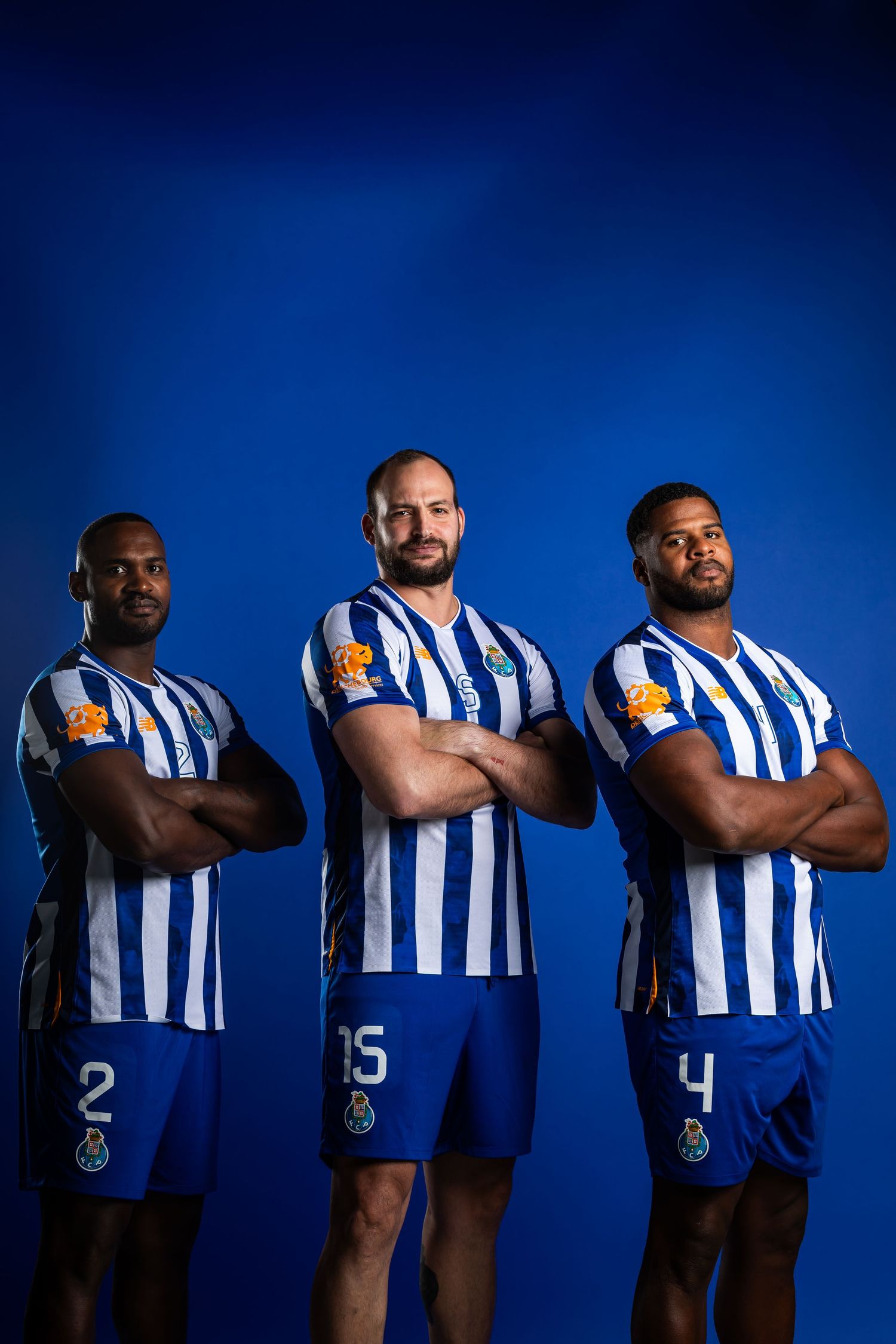 Three soccer players pose in blue and white striped uniforms against a dark blue background.