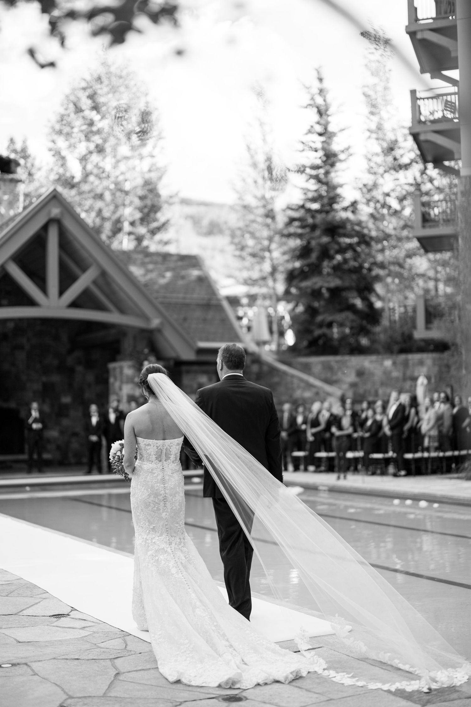 A romantic wedding ceremony moment by a pool with a flowing long veil.
