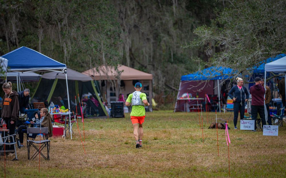 Runner in bright yellow shirt passes through race aid station with blue canopy tents.