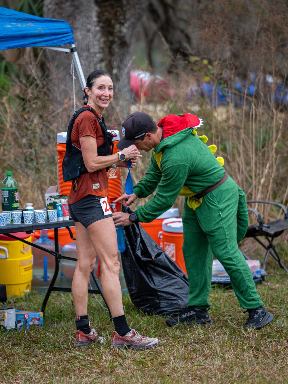 Trail race aid station with volunteers in costumes helping runners refuel.